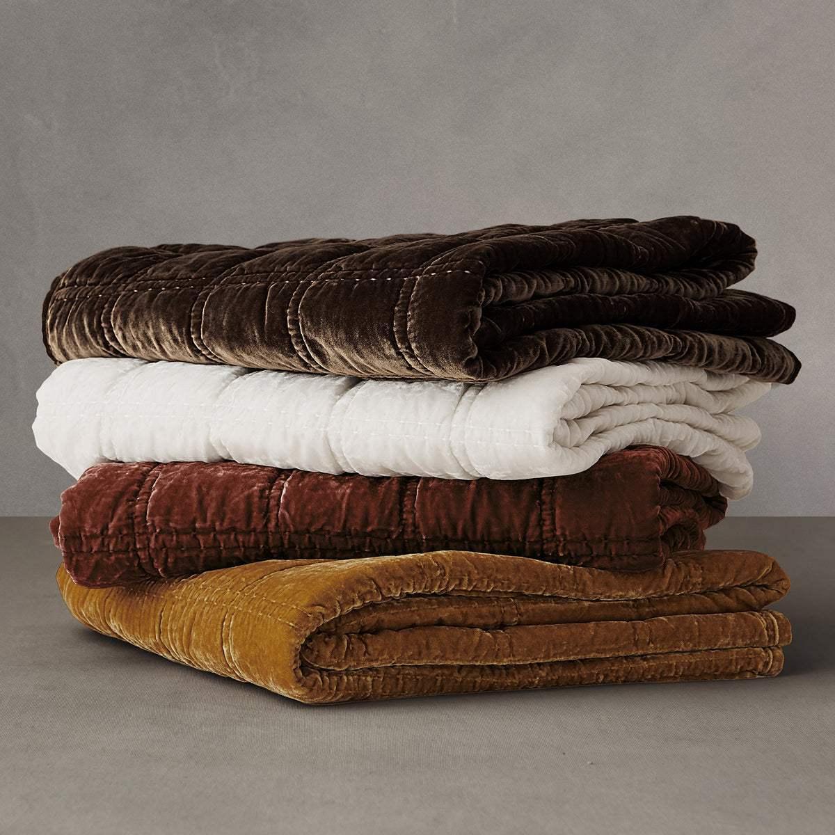 Four Stella velvet throws folded in a stack: espresso, ivory, garnet and ochre