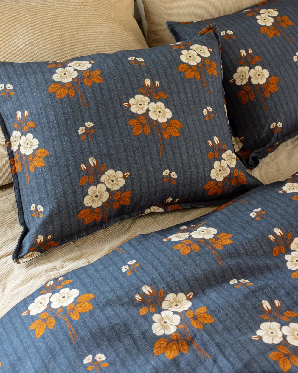 Close view of the folk floral print: cream and rust blossoms on a denim-blue ground with a tan corduroy pillow behind