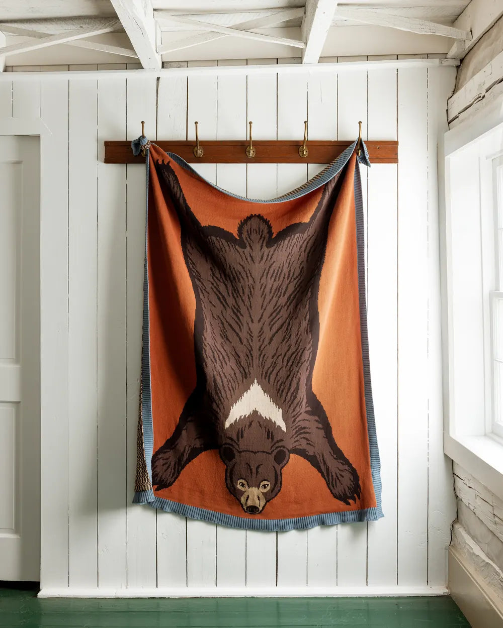 Sweater-knit throw in the shape of a bear hide, rust and brown, hanging from a peg rail